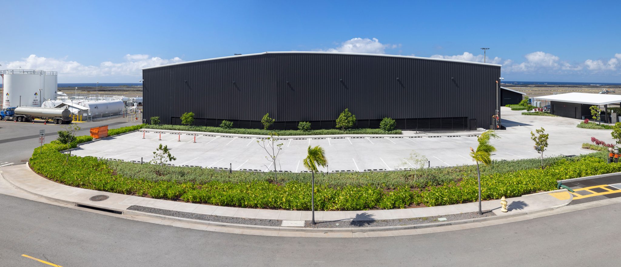 Pole‑aerial architectural photo of an industrial facility with storage tanks and coastal backdrop.